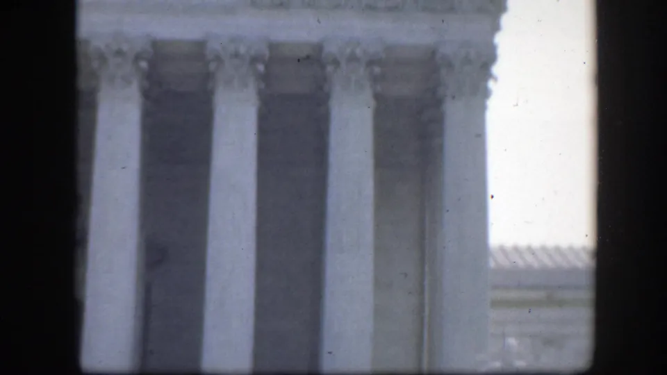 Handheld 8mm frame showing a tight crop of Washington DC monumental columns with bright overexposure along one side.