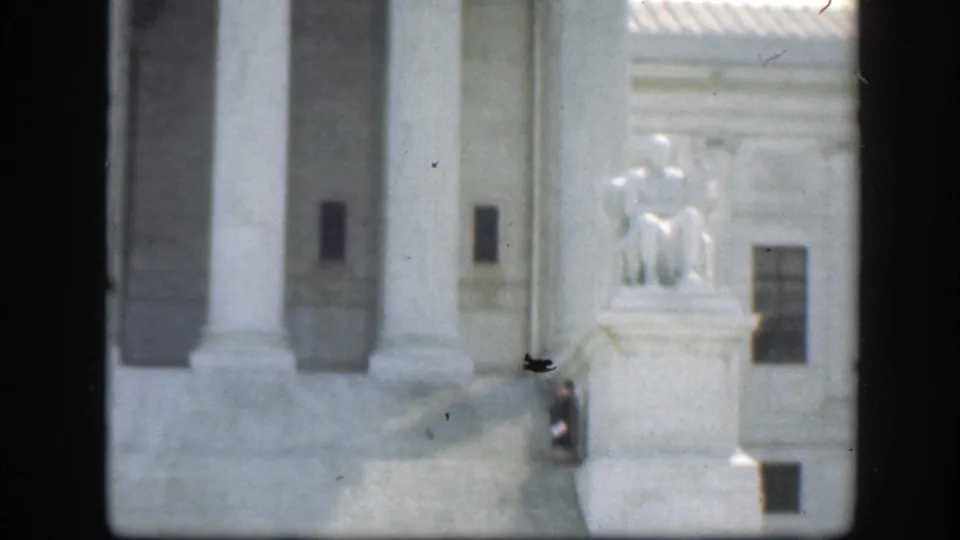 Washington DC federal landmark exterior with columns, steps, windows, and a seated statue visible to the right in soft 8mm footage.