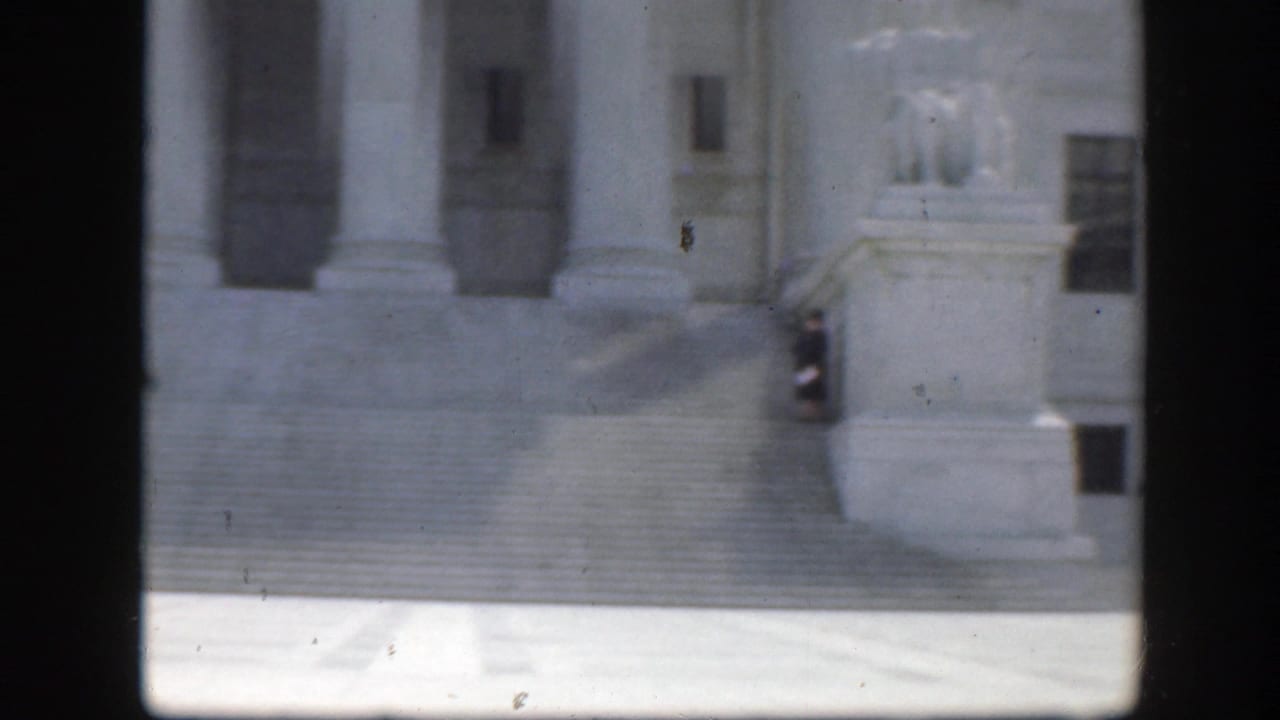 Classical building steps and columns seen through dark window-like divisions.