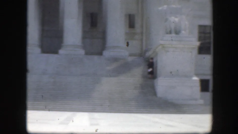 1945 Washington DC home-movie frame showing a white classical facade with columns, steps and a small figure near a statue.