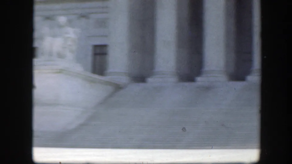 Soft 8mm view of a Washington DC classical building facade, with stone steps and large columns partly obscured by dark framing.
