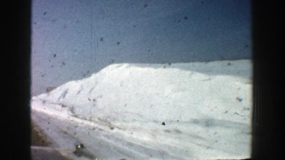 Car-window view of a large snowbank along a snowy highway near Aspen, Colorado, in metadata-supported 1961 footage.
