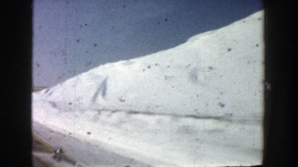 1961 Aspen-area road footage showing a high, bright snowbank passing close to the camera beneath a pale blue winter sky.