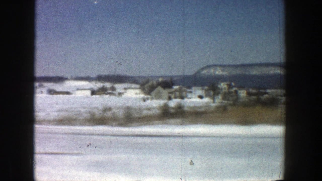1961 8mm view from a moving vehicle near Aspen, Colorado, showing snow-covered ground, distant houses, and a mountain ridge.