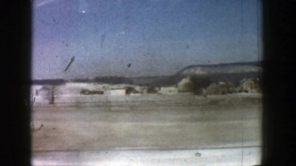 Passing 8mm frame from Aspen, Colorado, with snowy open ground, small distant structures, and a dark mountain ridge.