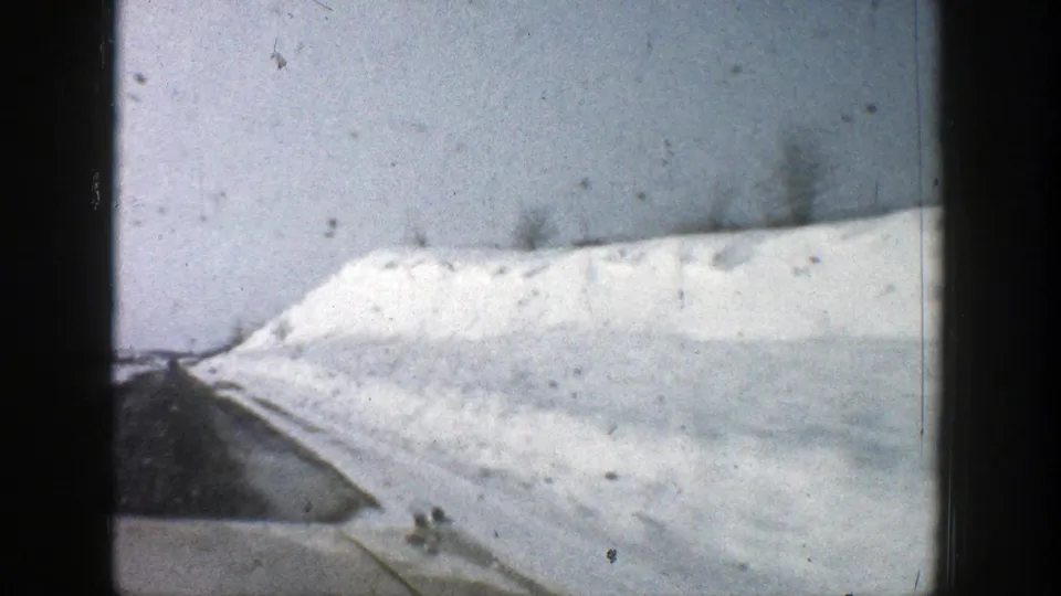 Moving-vehicle 8mm frame near Aspen, Colorado, showing a tall roadside snowbank and plowed highway edge.