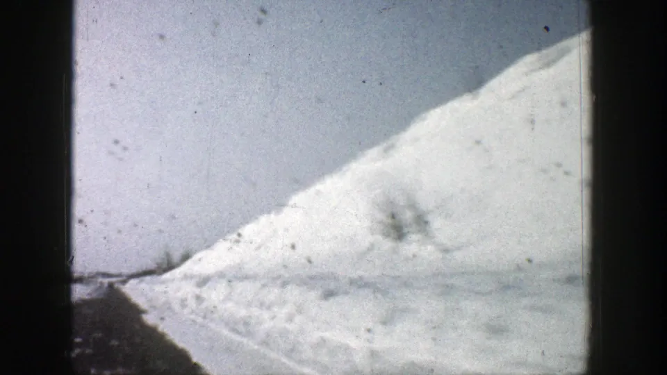 1961 8mm Aspen, Colorado view of a snow-covered hillside and roadside snowbank, filmed through a soft, grainy home-movie frame.