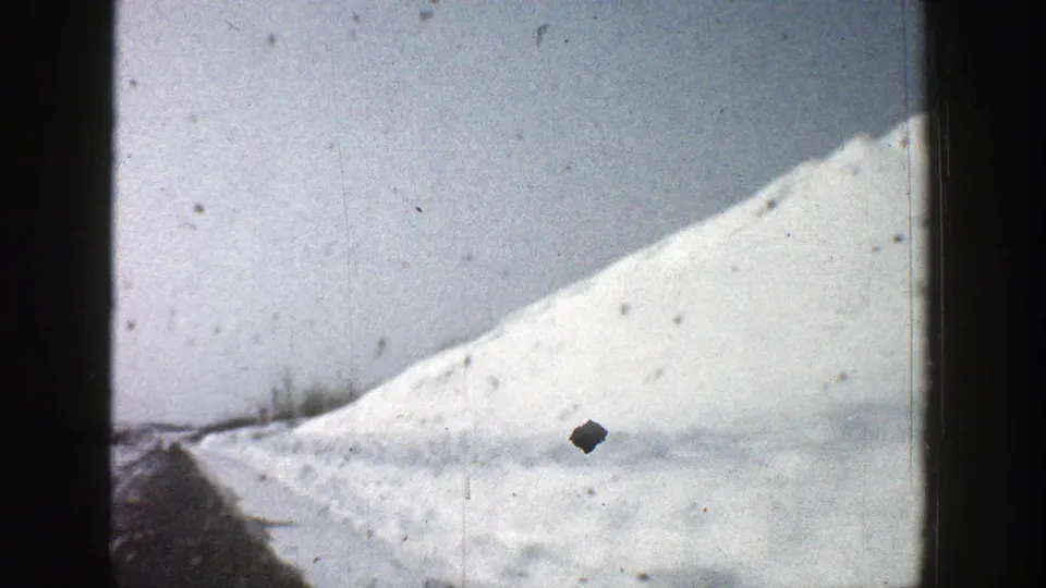 1961 8mm Aspen, Colorado frame showing the vehicle passing a sloped snowbank and dark roadside strip under a pale winter sky.