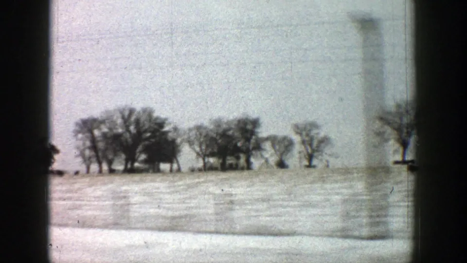 1961 Aspen, Colorado area home-movie view of a snowy rural field, bare trees, and distant buildings through a moving vehicle window.