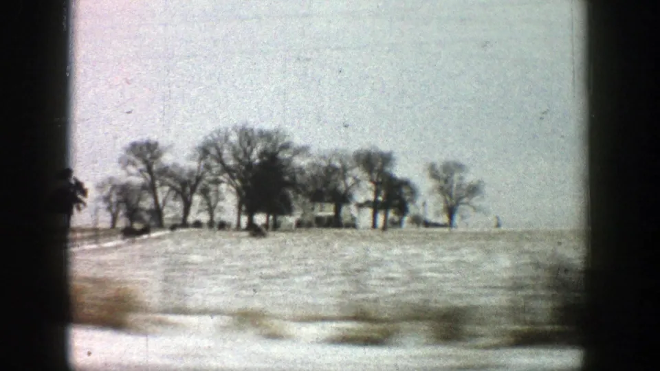 Rural Aspen, Colorado area landscape from 1961 with snow-covered ground, leafless trees, and distant farm structures filmed from a vehicle.