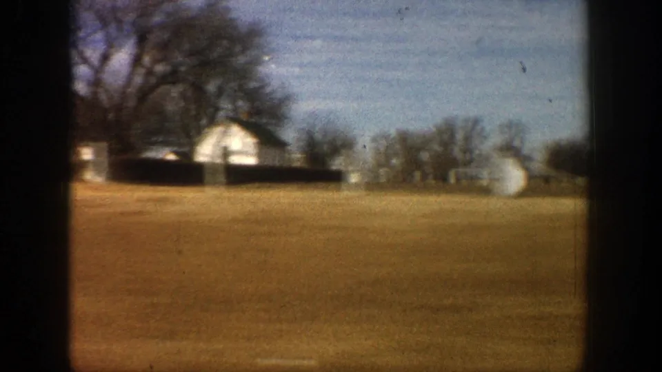 A white rural house and outbuildings appear beyond open fields in the 1961 Aspen, Colorado home-movie drive.