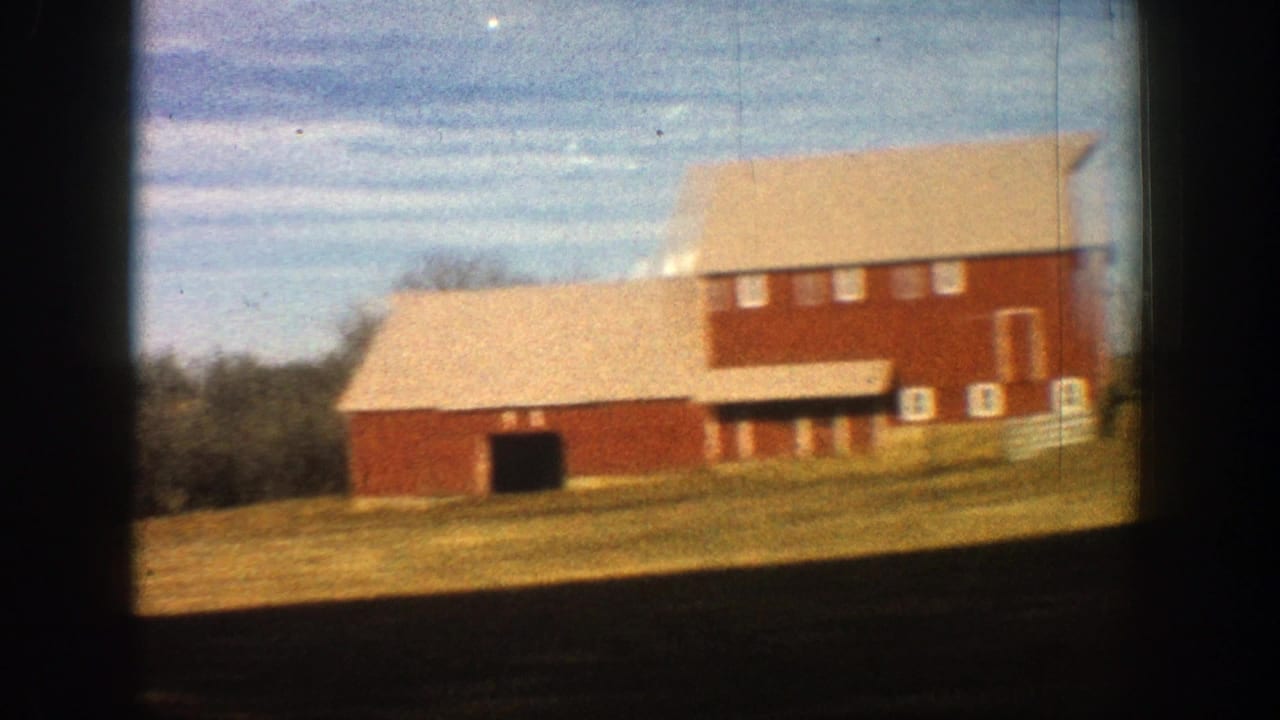 1961 Aspen, Colorado 8mm frame showing red farm buildings with pale roofs and white trim beside open rural ground.