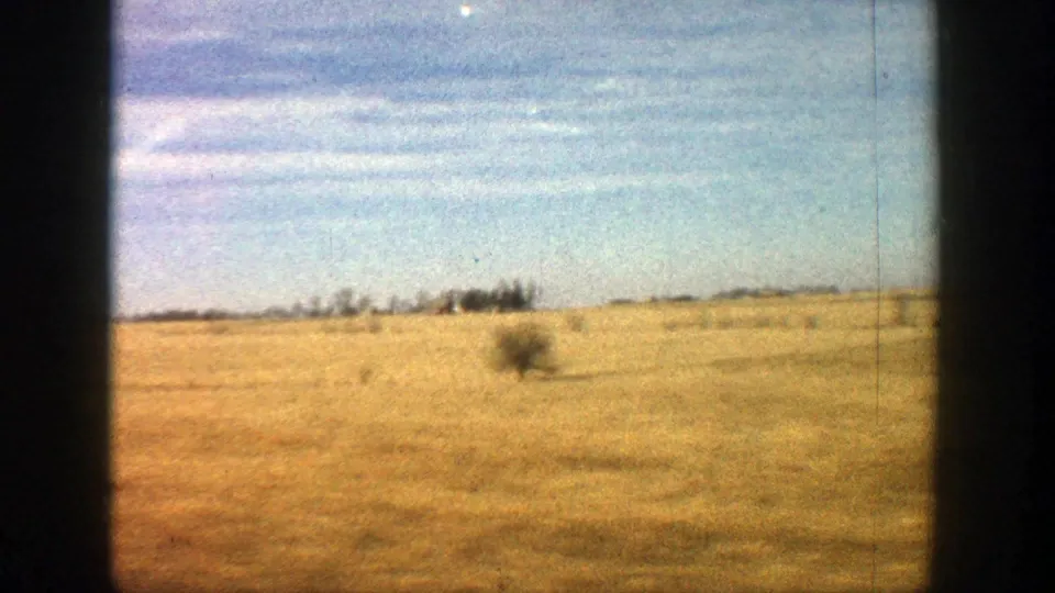 Rural Aspen, Colorado 8mm view of a broad field, distant tree line, and bright sky as the moving camera clears the farm buildings.