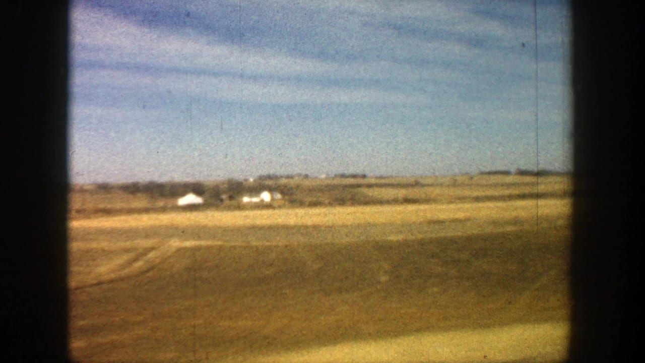 Distant white houses across a broad brown plain beneath blue sky.
