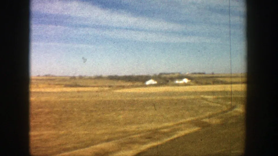 Vintage 8mm view near Aspen, Colorado, showing open grassland, faint tracks, and small houses on the horizon.