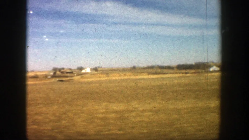 1961 8mm view of a rural Aspen-area field with distant structures, blue sky, and dark frame borders from the film gate.