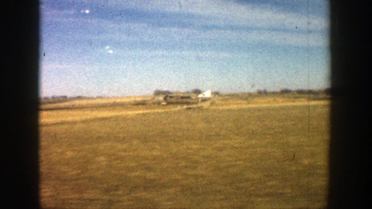 Open field and distant farm buildings viewed through dark film-gate borders.