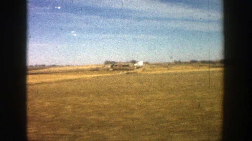 Rural Aspen, Colorado landscape from 1961 home-movie footage, with open grassland, distant structures, and pale blue sky.
