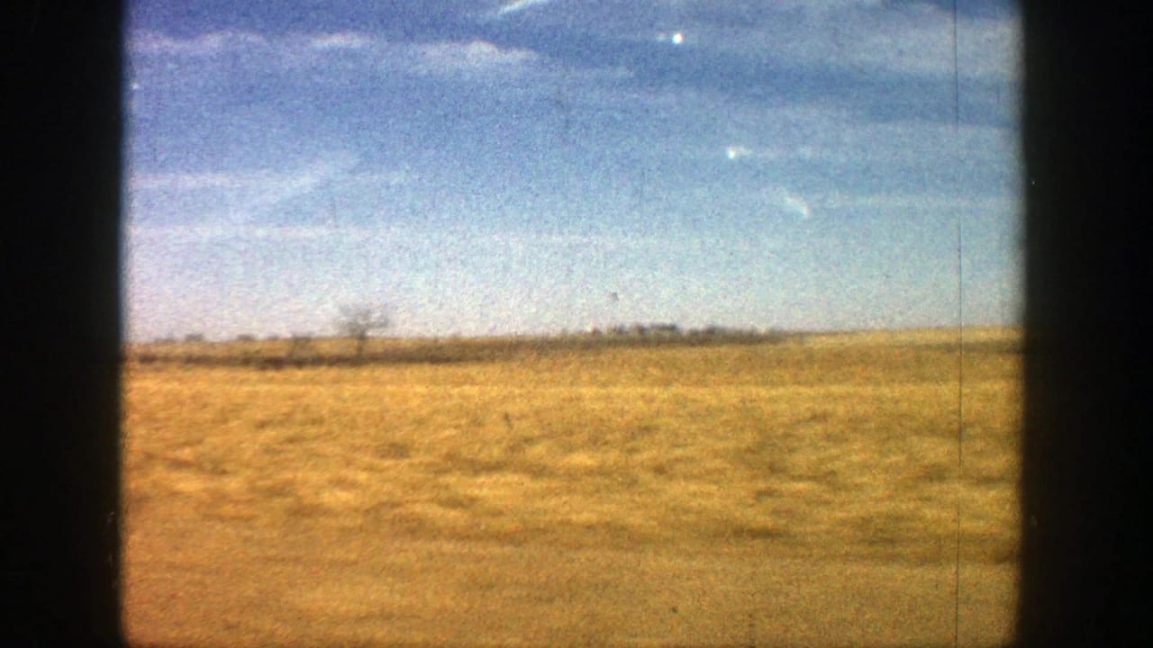 Dry open field beneath a blue sky, framed by dark 8mm film borders.
