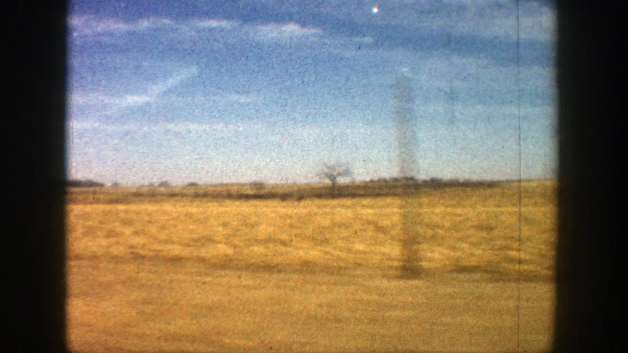 Dry field and distant horizon under a blue sky within dark film borders.