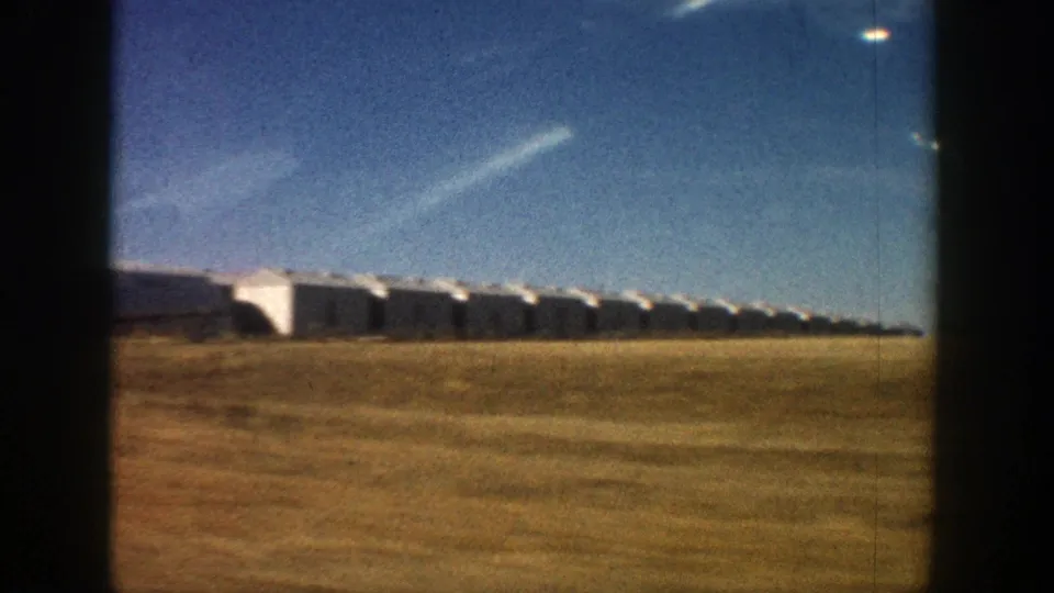 1961 Aspen-area moving-car frame showing a long row of white low buildings beside dry open ground.