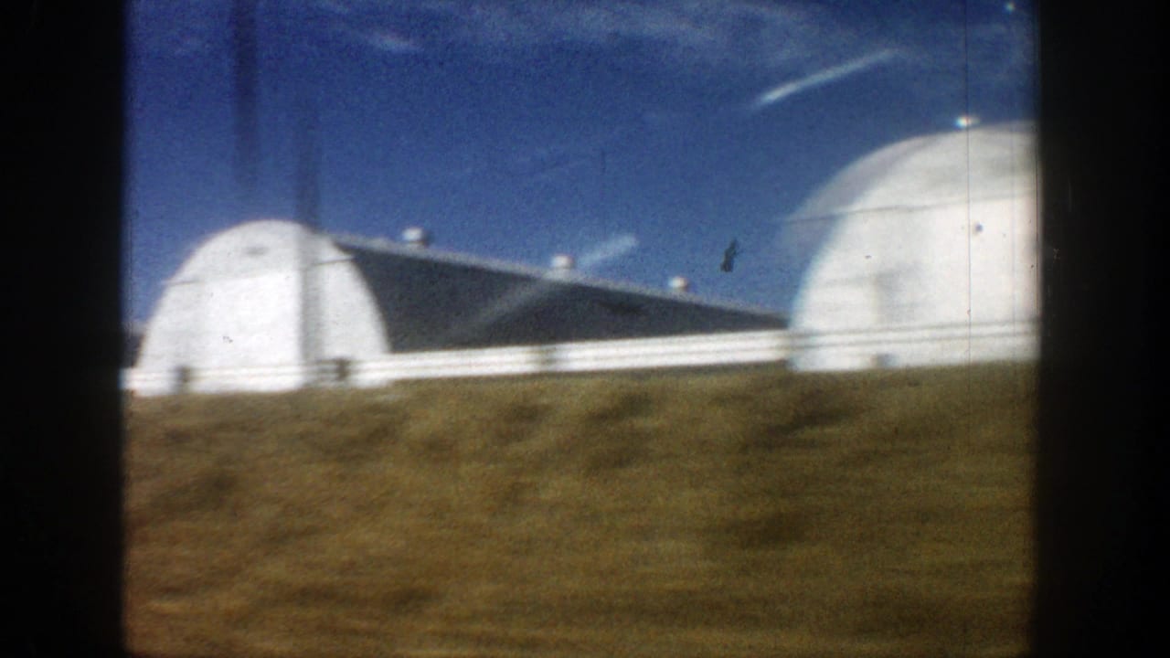 Rounded white farm structures and a long building behind grassy ground.