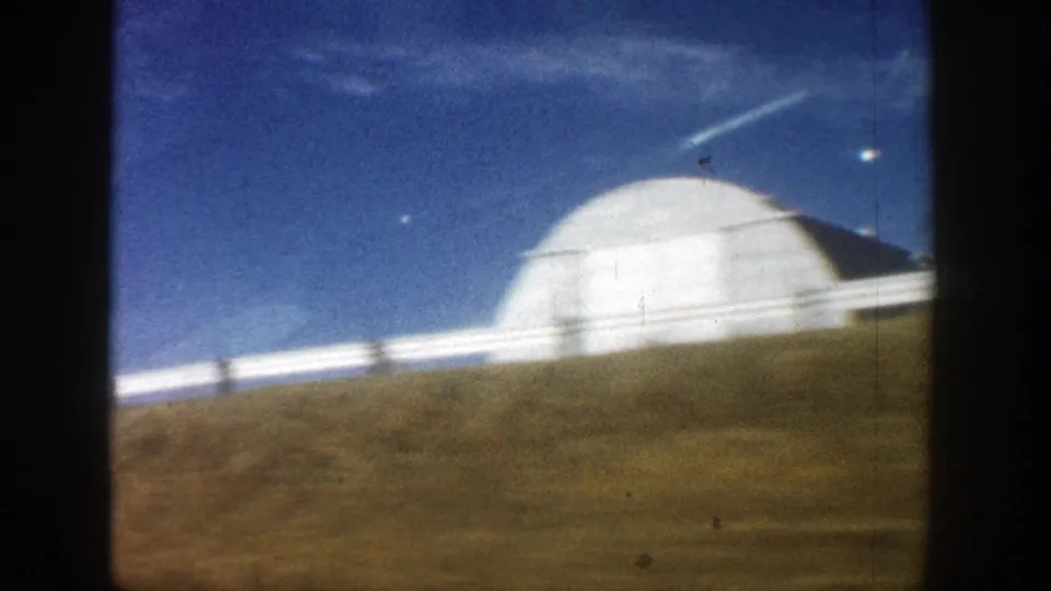 Motion-blurred 1961 Aspen-area 8mm frame with a rounded white farm building and open grassland.