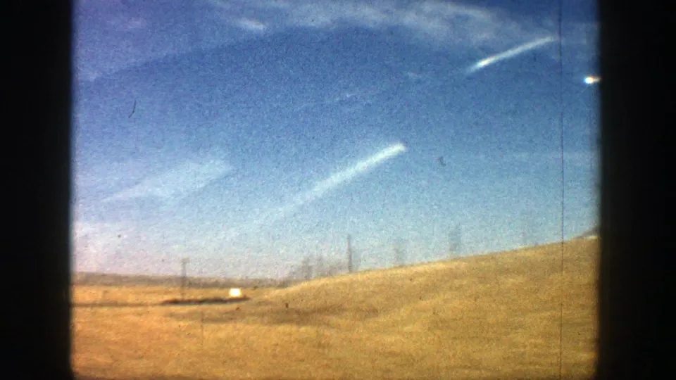 1961 Aspen 8mm frame showing open grassland, fence posts, and sky after the farm buildings pass out of view.