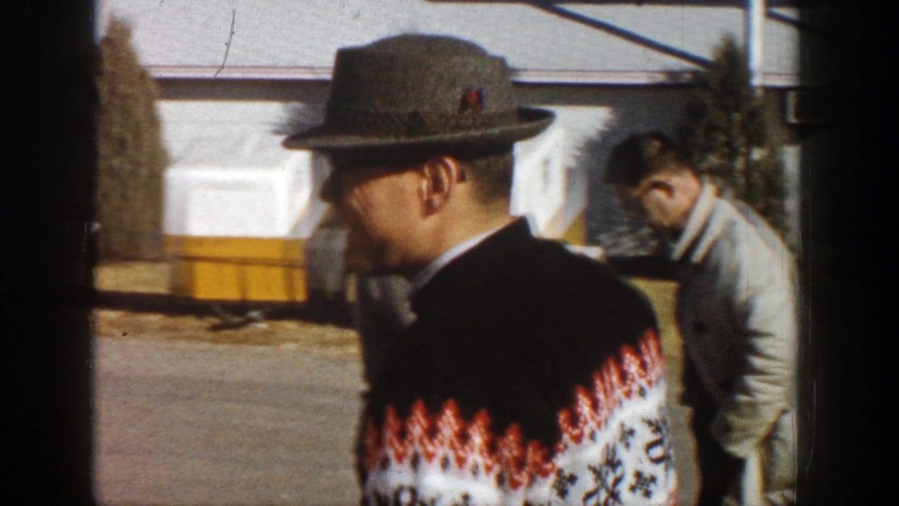 Man in patterned sweater turns away while another man stands nearby outdoors.