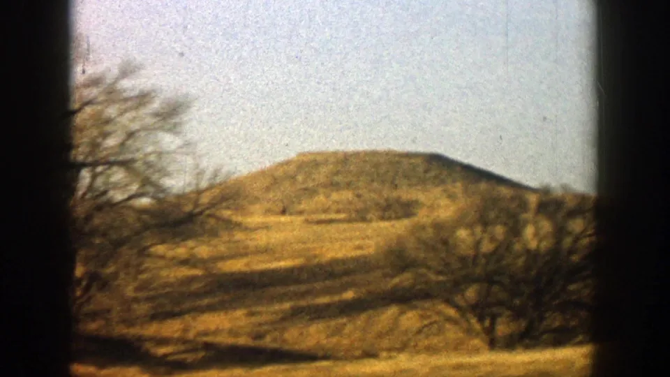 Handheld 1961 Aspen, Colorado landscape frame with a low hill, bare trees and warm 8mm color.