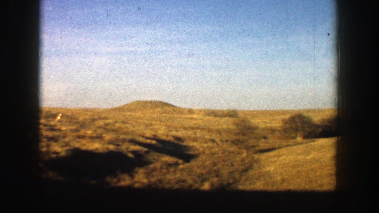 Open scrubland and a low hill pass by beneath a clear blue sky.