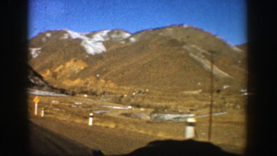 1961 Aspen, Colorado 8mm view of mountain foothills, roadside posts, utility pole, and a valley floor seen from a moving car.