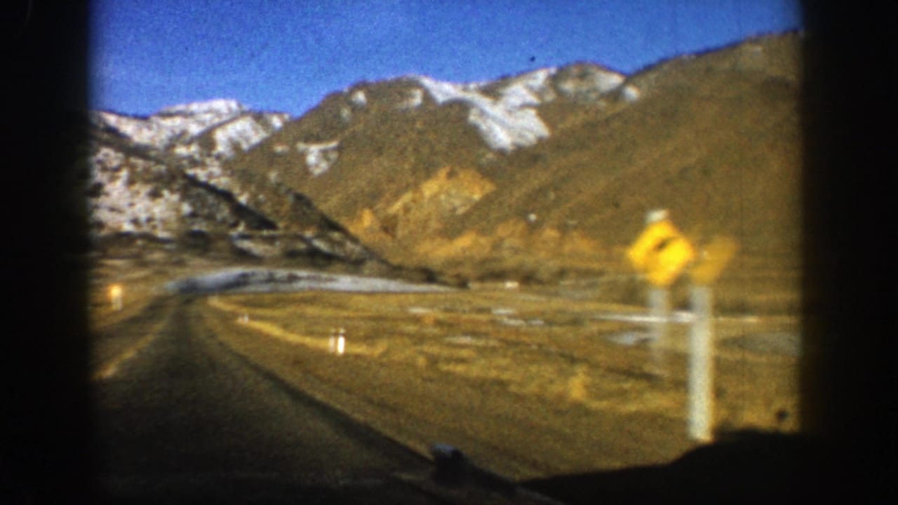1961 Aspen, Colorado travel footage showing a road curving through mountains, framed by dark car-window edges.