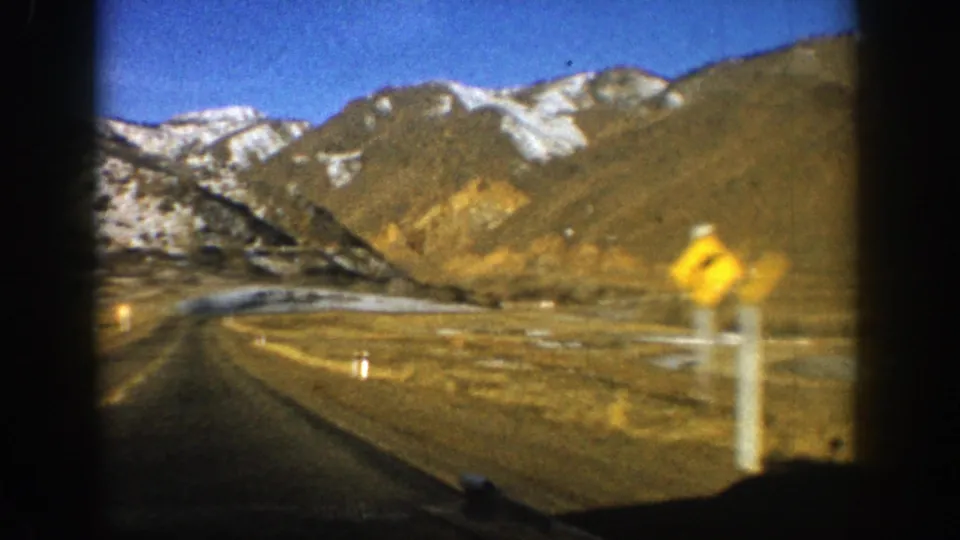 1961 Aspen, Colorado travel footage showing a road curving through mountains, framed by dark car-window edges.