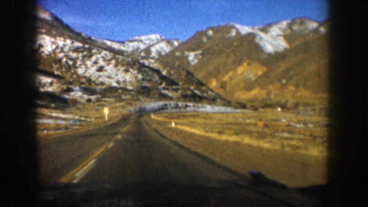 Open mountain highway leading toward snow-dusted peaks under a blue sky.