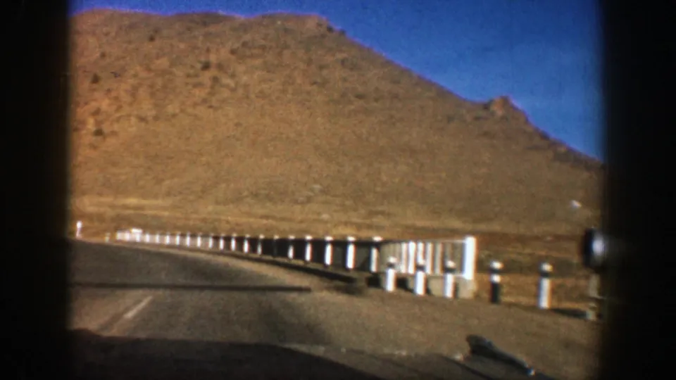 1961 Aspen-area car-window footage showing a road curve, white guardrail posts, and an arid mountain hillside.
