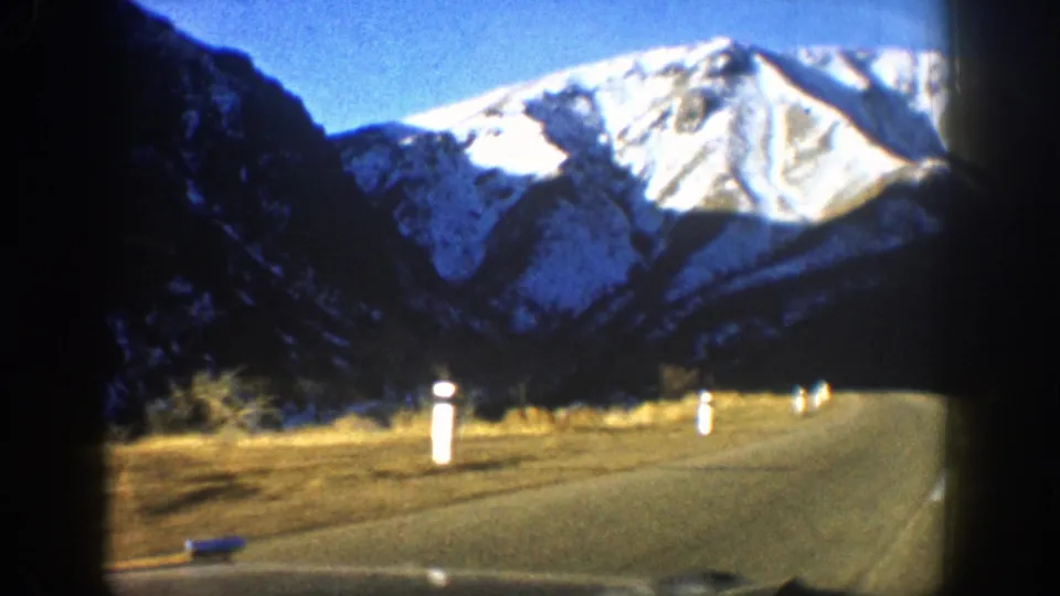 1961 8mm home-movie frame showing an open road through a Colorado valley below snowy mountains near Aspen.