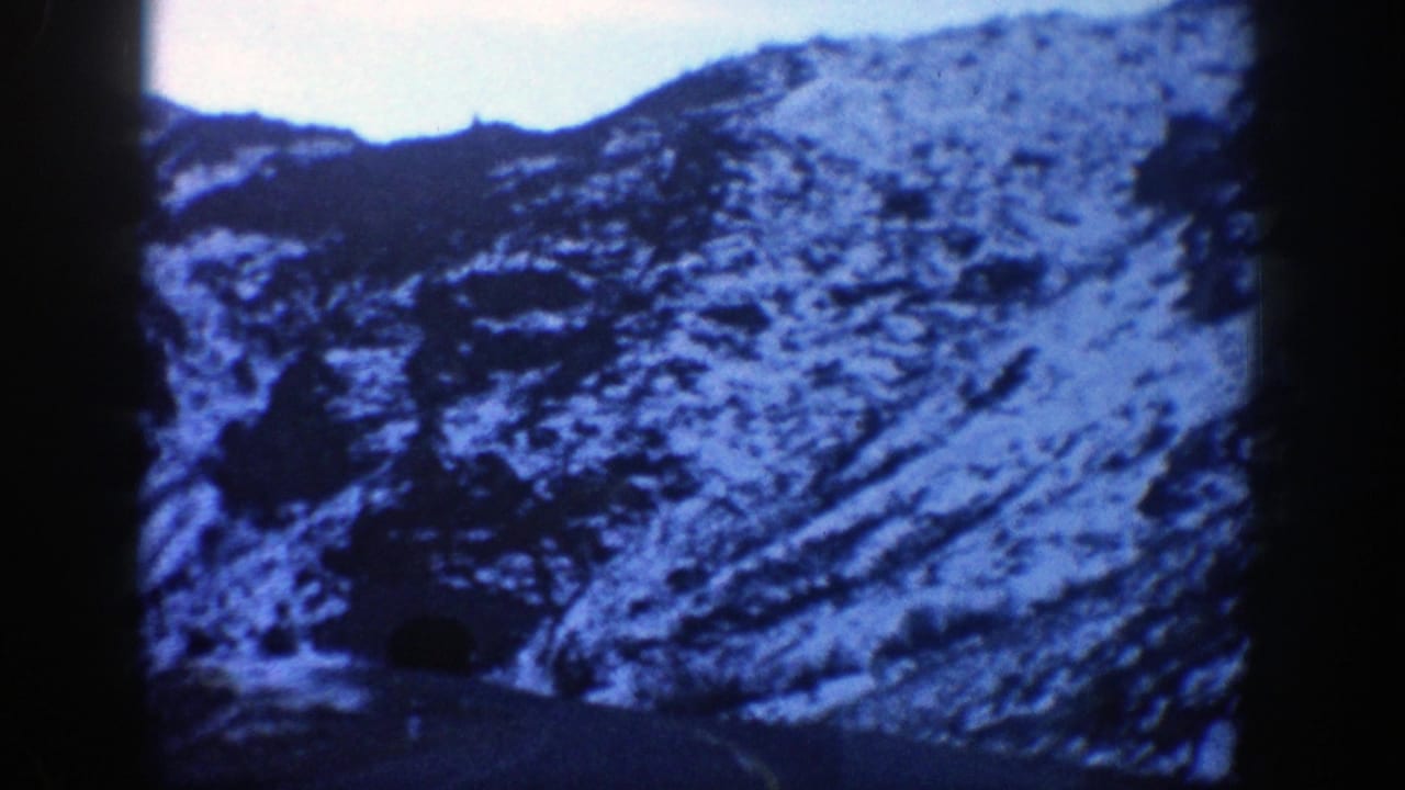 1961 Aspen, Colorado 8mm frame showing a snowy mountain slope and road approaching a dark tunnel entrance.
