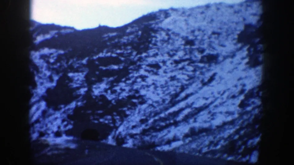 1961 Aspen, Colorado 8mm frame showing a snowy mountain slope and road approaching a dark tunnel entrance.