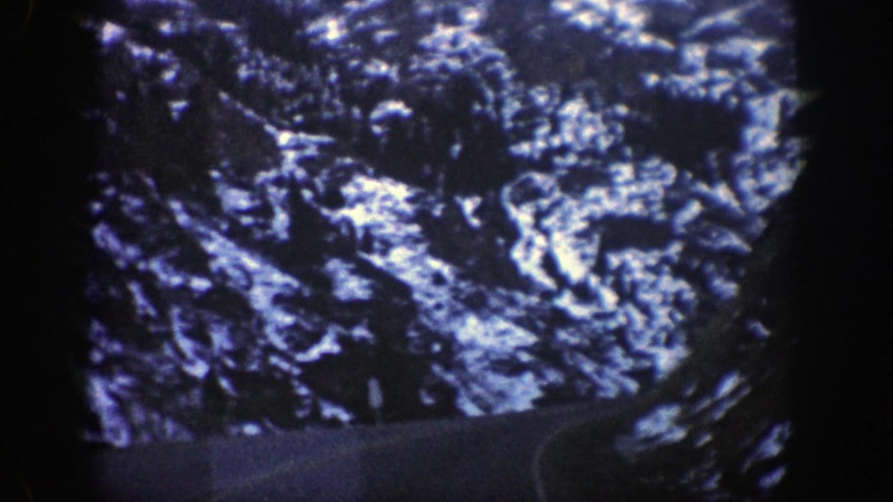 1961 8mm view of a winding mountain road near Aspen, Colorado, bordered by dark canyon slopes and patches of snow.