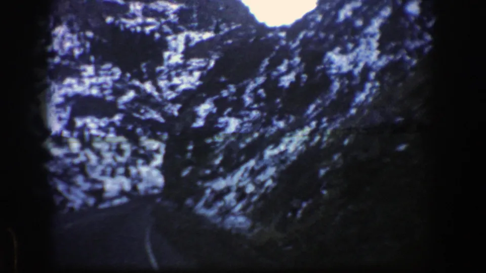Soft 8mm frame of a winter mountain road near Aspen, with the lane curving through shadowed rock walls and snow.