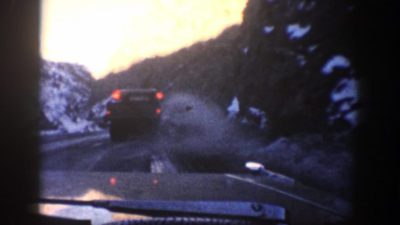 1961 Aspen-area 8mm view from inside a car following another vehicle on a snowy mountain road.