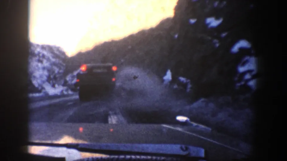 1961 Aspen-area 8mm view from inside a car following another vehicle on a snowy mountain road.
