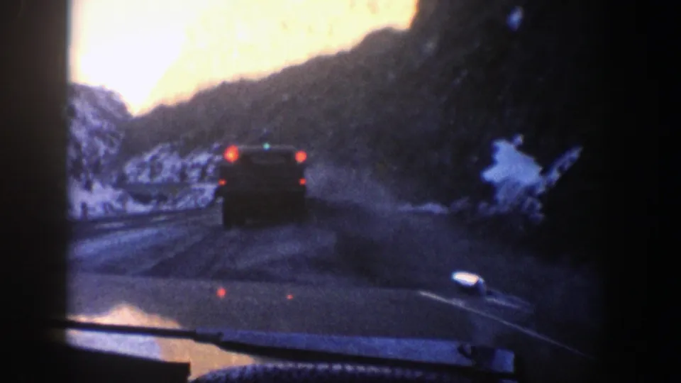 In-car 8mm view of a dark vehicle ahead on a winding snowy road in the Aspen, Colorado area.