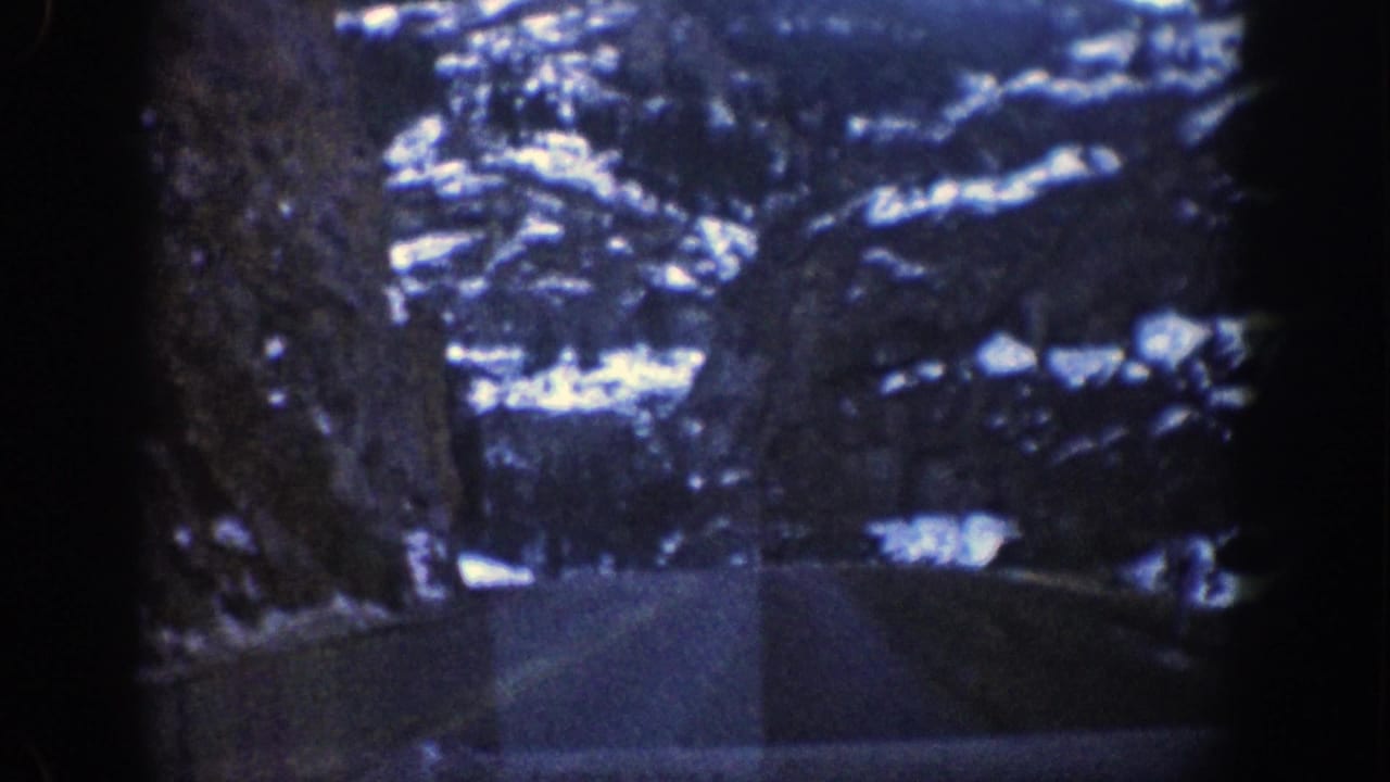 Snowy mountain road passing between dark rocky slopes and evergreen trees.