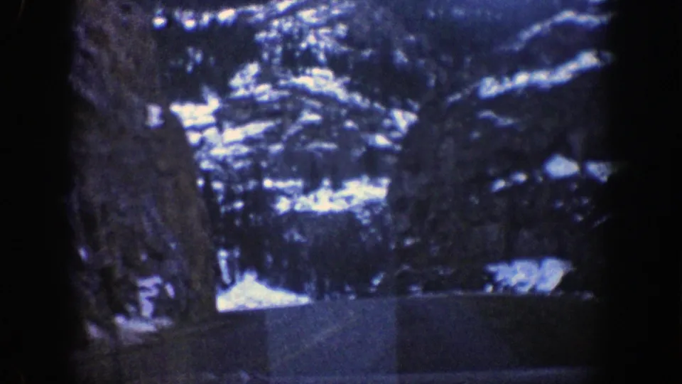 A 1961 Aspen road-view frame shows a paved route through snow-dusted rock faces and dense evergreens.