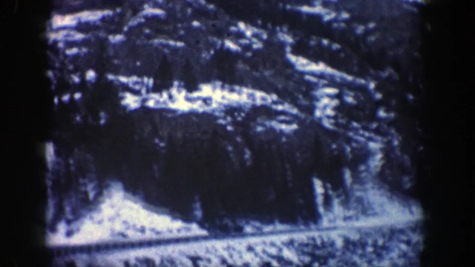 A late-frame 1961 Aspen road view shows snowbanks, dark evergreens, and rocky mountain terrain beside the roadway.