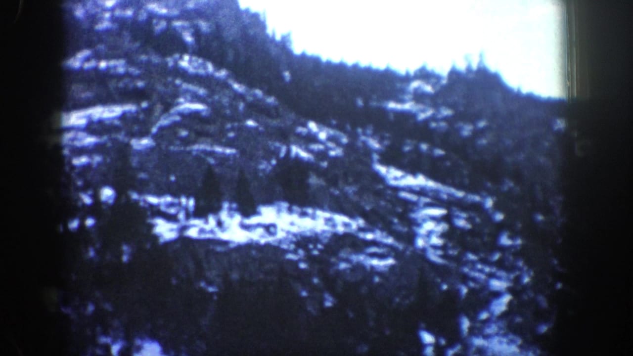 Snow-dusted rocky mountain slope with evergreen trees seen through a dark film frame.