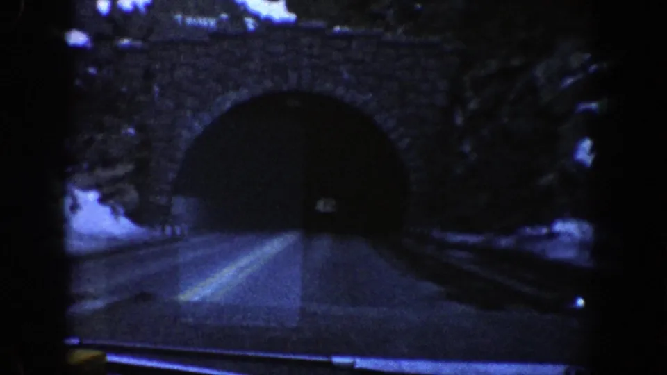 End frame of the 1961 Aspen, Colorado drive clip showing the car nearing a dark stone tunnel entrance on a mountain road.