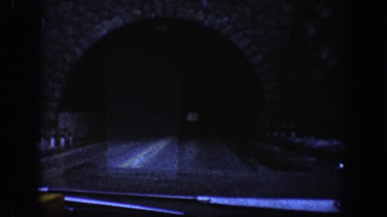 Dark stone-arch highway tunnel entrance seen from inside a moving car.
